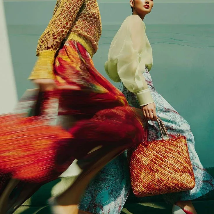 Model in a flowing printed skirt with a woven bag, mid-stride